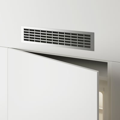 Rechteckiges Lüftungsgitter aus Metall, das an einer weißen Wand über einer Türöffnung montiert ist und den Luftstrom ermöglicht.