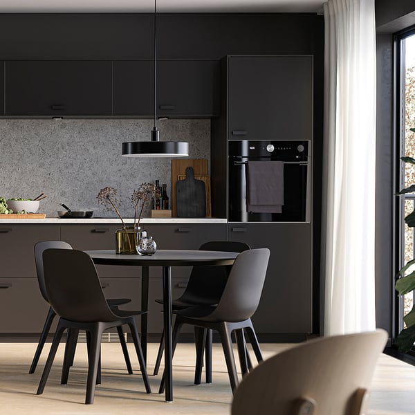 Moderne Küche mit METOD-Schränken in mattem Schwarz. Enthält einen eingebauten Backofen, einen eleganten Esstisch und Stühle.