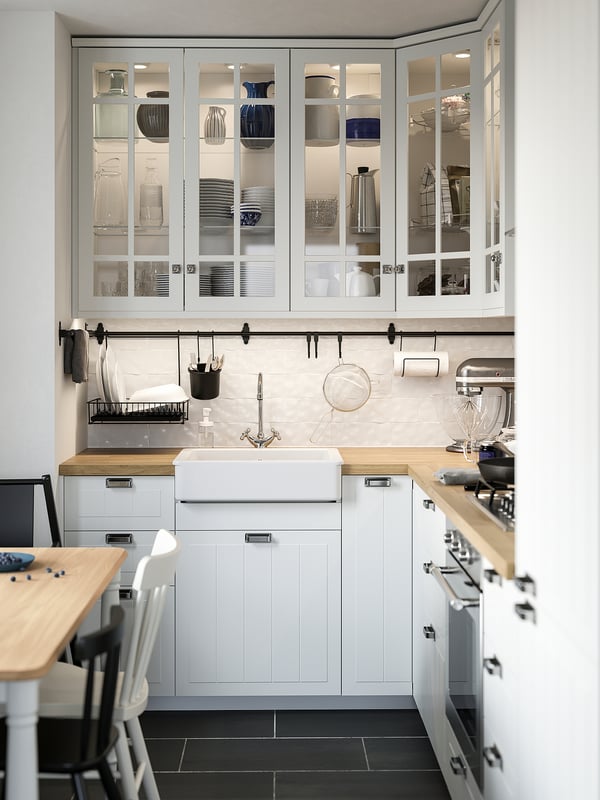Moderne weiße Küche mit Glasfrontschränken, Holzarbeitsplatten, Holztisch und schwarzem Boden.