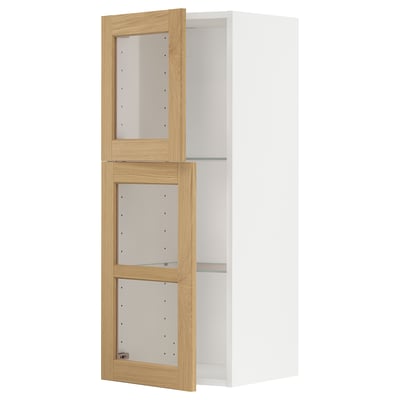 Ein weißer METOD-Küchenschrank mit Glastüren aus Eichenholz, verstellbaren Regalen und abgeschrägten Kanten.
