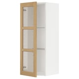 Ein weißer METOD-Küchenschrank mit verstellbaren Regalen und einem hellen Holzrahmen. Es Glastüren mit Eichenfurnier.