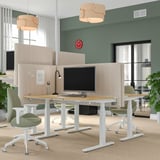 Modernes Büro mit MITTZON Schreibtischschirmen, grünen Stühlen und natürlichem Licht durch große Fenster. Die rote Uhr sorgt für Farbe und minimale Ablenkungen für die Konzentration.