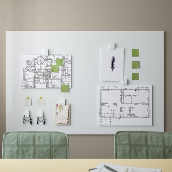 Ein Whiteboard mit grünem Rahmen und grünen Stühlen. Die Tafel zeigt Architekturpläne und bunte Haftnotizen, die eine Arbeitsbereichseinrichtung hervorheben.