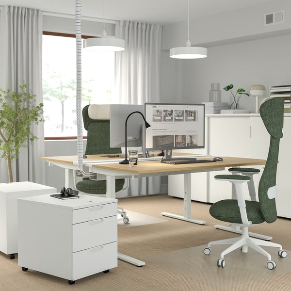Modernes Homeoffice mit verstellbarem MITTZON-Schreibtisch, grünem Stuhl und weißem Stauraum. Helle Holzplatte, weißer Rahmen, geräumig, mit Monitor und Zubehör.