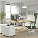 Modernes Homeoffice mit verstellbarem MITTZON-Schreibtisch, grünem Stuhl und weißem Stauraum. Helle Holzplatte, weißer Rahmen, geräumig, mit Monitor und Zubehör.