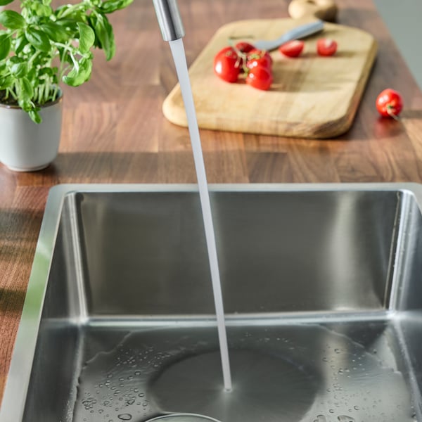 Küchenspüle mit fließendem Wasser, Pflanzen und Schneidebrett mit Tomaten.