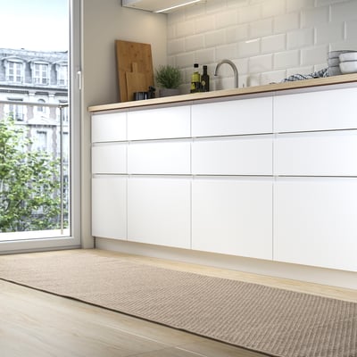 Moderne Küche mit weißem MORUM-Teppich , hellen Holzböden, Flussarbeitsplatten und eleganten Schränken am Fenster.