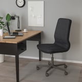 Einrichtung des Home-Office: schwarzer MULLFJÄLLET-Stuhl, Schreibtisch aus Holz, Laptop, Lampe, Pflanze und Wandkunst.