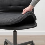 Eine Hand kippt die Rückenlehne eines grauen MULLFJÄLLET-Bürostuhls und zeigt so die verstellbare Kippspannung.