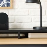 Moderner Schreibtisch mit schwarzer Lampe, Lautsprecher und Büchern, die auf einen funktionalen Arbeitsplatz hinweisen.