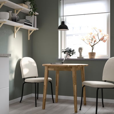 Moderne, minimalistische Esseinrichtung mit NACKANÄS, rundem Tisch aus Akazienholz und weißen Stühlen. Eingebaute Regale halten die Dekoration fest. Natürliches Licht durch großes Fenster.