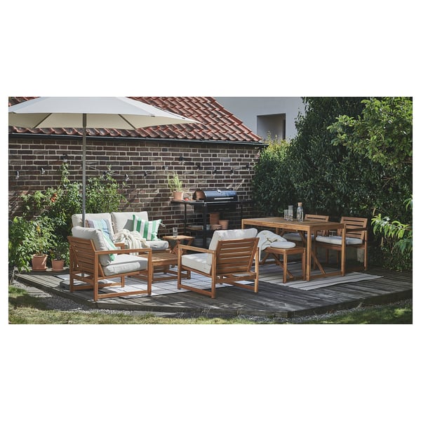 Gartenmöbel für den Außenbereich mit Holztisch, Stühlen und Sofa unter einem beigen Sonnenschirm, angeordnet auf einer Holzterrasse in der Nähe eines Backsteinhauses.