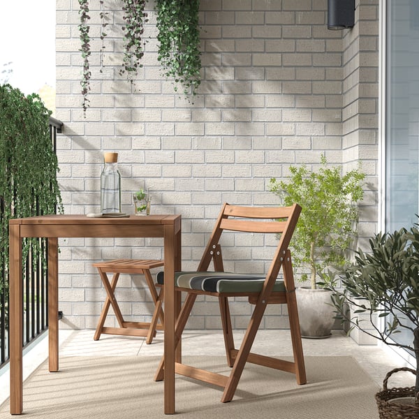 Holzterrasse mit Tisch und gestreiften Stühlen an einer Wand mit Pflanzen.
