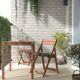 Holzterrasse mit Tisch und gestreiften Stühlen an einer Wand mit Pflanzen.