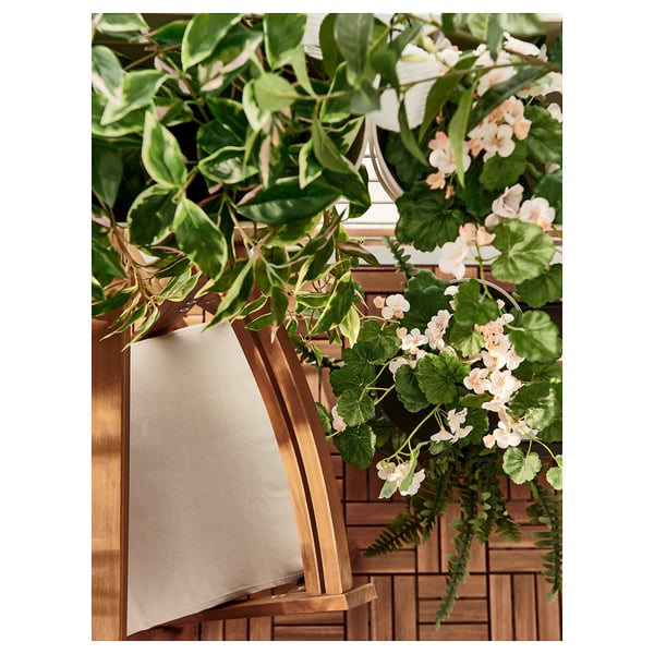 Outdoor-Setup mit beigem NÄMMARÖ-Stuhl, üppigen grünen Pflanzen und weißen Blumen.