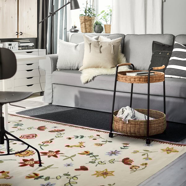 Gemütliches Wohnzimmer mit grauem Sofa, buntem Blumenteppich und Beistelltisch aus Korbgeflecht.