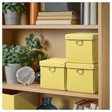Holzregal mit drei gelben NIMM Organizer-Boxen, Pflanzen und Büchern.