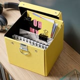 Ein gelber Organizer mit Notizkarten und Heftklammern auf einem Holztisch, daneben ein schwarzes Headset.