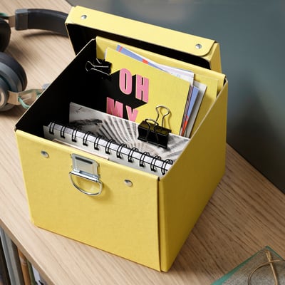 Ein gelber Organizer mit Notizkarten und Heftklammern auf einem Holztisch, daneben ein schwarzes Headset.