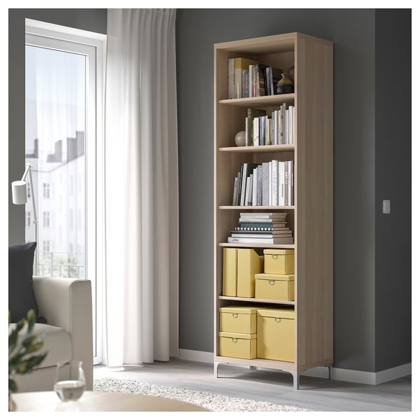 Hohes Bücherregal aus Holz mit mehreren Regalen, gefüllt mit Büchern und gelben Aufbewahrungsboxen. Positioniert in der Nähe eines Fensters mit durchsichtigen Vorhängen.