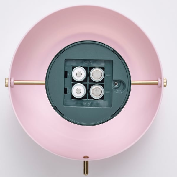 Eine batteriebetriebene LED-Lampe mit USB-C-Ladeanschluss, die auf einem rosafarbenen runden Sockel mit verstellbaren goldenen Stäben montiert ist.