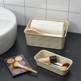 Badezimmertheke mit schwarzem Marmor, beigem Organizer mit Handtüchern und Bürsten sowie Make-up-Artikeln.