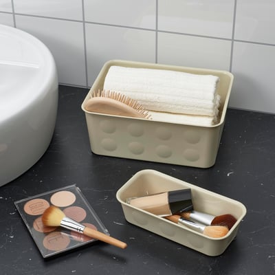 Badezimmertheke mit schwarzem Marmor, beigem Organizer mit Handtüchern und Bürsten sowie Make-up-Artikeln.