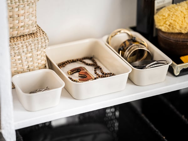 Weißes organisiertes Regal mit Schmuck in durchsichtigen Plastikboxen mit Halsketten, Ringen und Armbändern.