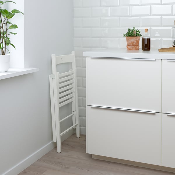 Minimalistische Küche mit NORDEN Tisch und Klappstuhl, Schubladen, Pflanze, Flasche.