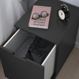 Nachttisch mit Decke, Buch und Uhr neben weißem Bett.