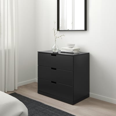 Moderne schwarze NORDLI Kommode mit 3 Schubladen, schlank und minimalistisch, passt in kompakte Räume. Gut platziert unter einem Spiegel, mit einem hohen weißen Vorhang in der Nähe.