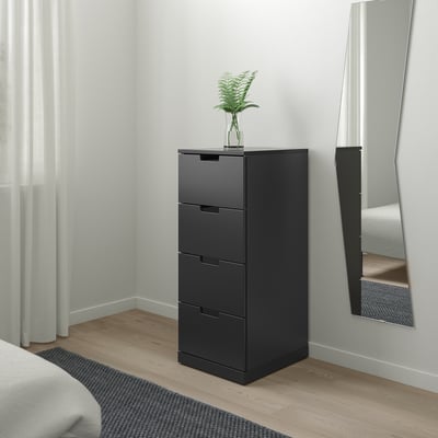Moderne schwarze NORDLI-Kommode mit drei Schubladen und einer Pflanze obendrauf, an einer Wand neben einem Spiegel in einem minimalistischen Schlafzimmer positioniert.