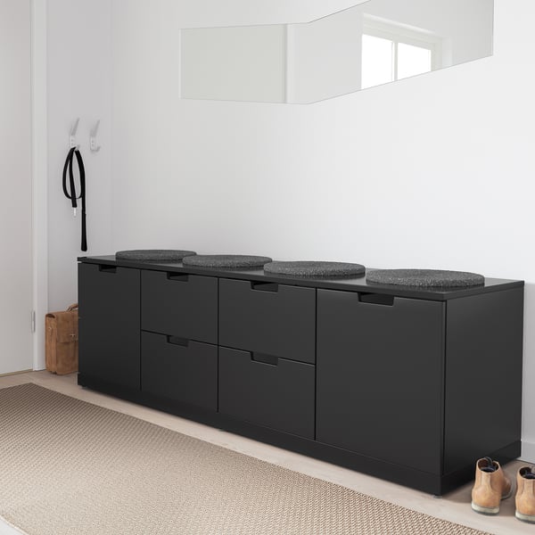 Eine schwarze NORDLI-Kommode mit vier Schubladen, Kissen und Schuhregal daneben.