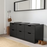 Eine schlanke schwarze NORDLI-Kommode mit sechs minimalistischen Schubladen, einem Spiegel darüber und kleinen Gegenständen in der Nähe.