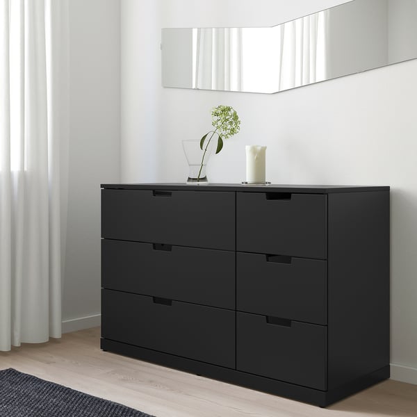 Schwarze NORDLI Kommode mit 6 Schubladen an weißer Wand.