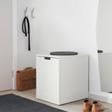 Moderne weiße NORDLI Truhe mit grauem Kissen, neben dem Eingang mit Willkommensmatte, Tasche und Schuhablage.