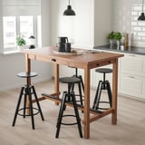 Ein NORDVIKEN Küchentisch und Stühle. Hellbraunes Oberteil, dunkle Beine, schwarze Sitze. Bietet Platz zum Essen, Stauraum in einer Schublade und Haken. Modern, minimalistisch.