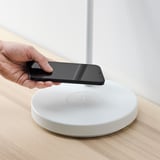 Person, die das Smartphone auf ein weißes kabelloses Ladepad auf einem Holzschreibtisch legt.