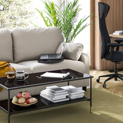 Moderner Wohnbereich mit grauem Sofa, schwarzem Laptop-Tablett, grünem Teppich und Holzboden.