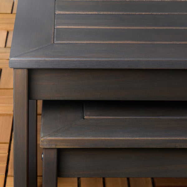 Dunkelbrauner Outdoor-Tisch aus Holz mit schlanken, glatten Kanten und sichtbarer Holzmaserung, der an einer Ziegelwand steht.