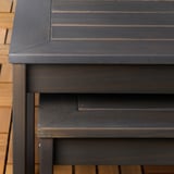 Dunkelbrauner Outdoor-Tisch aus Holz mit schlanken, glatten Kanten und sichtbarer Holzmaserung, der an einer Ziegelwand steht.