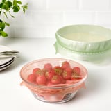 Zwei Glasschalen mit Deckel: eine mit frischen Erdbeeren, eine mit Sahne. Die Schalen stehen auf einer weißen Arbeitsplatte.