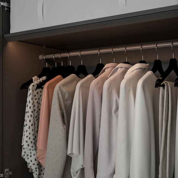Ein moderner Kleiderschrank mit LED-Lichtstreifen, die Kleidung auf Kleiderbügeln beleuchten. Das Licht passt sich automatisch an die Position der Tür an.
