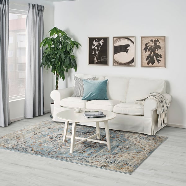 Modernes Wohnzimmer mit OVERLUND-Teppich, weißem Couchtisch und Sofa mit blauen/schwarzen Kissen.