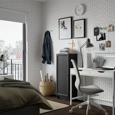 Minimalistisches Homeoffice mit grauem OXBERG-Bücherregal, weißem Schreibtisch, grünem Bett und Wandkunst.