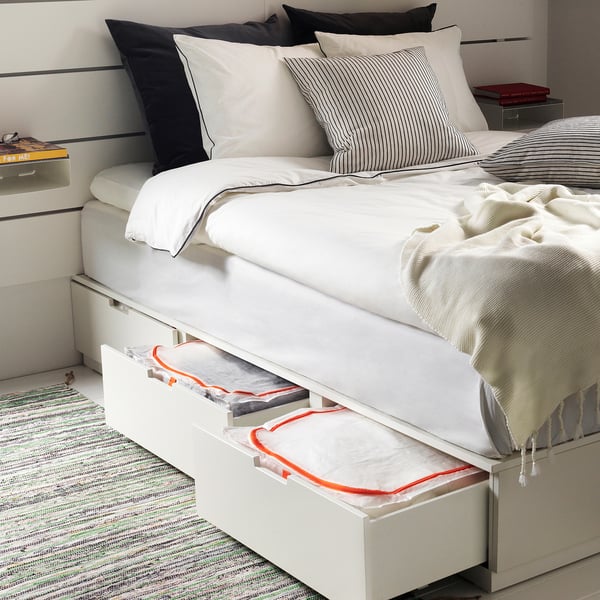 Schlafzimmer mit PÄRKLA Leinensack unter dem Bett, rotem Reißverschluss, gestreiften Kissen, Buch, Lampe.