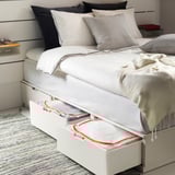 Schlafzimmer mit PÄRKLA Leinensack unter dem Bett, rotem Reißverschluss, gestreiften Kissen, Buch, Lampe.