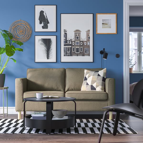 Modernes Wohnzimmer: beiges Sofa, schwarzer Couchtisch, gestreifter Teppich, blaue Wand mit Kunst und Pflanzen.