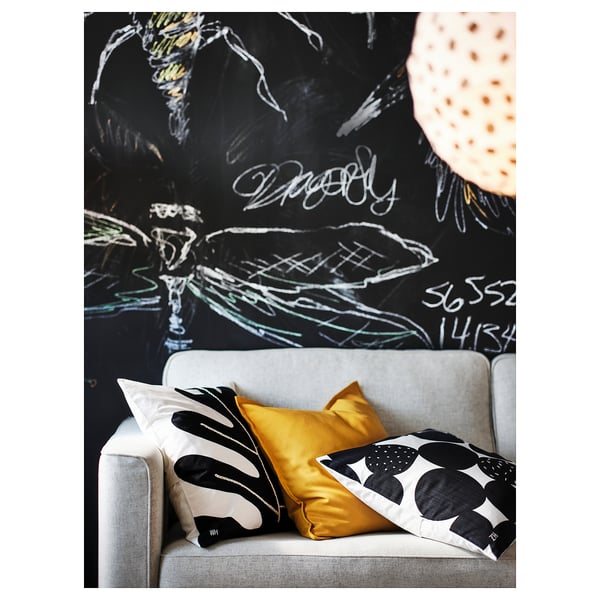 Das PÄRUP-Sofa mit bunten Kissen vor einer fetten, schwarzen Wand mit weißem Graffiti.
