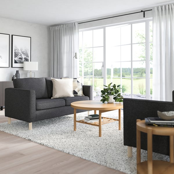 Modernes Wohnzimmer mit großem Fenster, grauem PÄRUP-Sofa, Couchtisch aus Holz und gesprenkeltem Teppich.